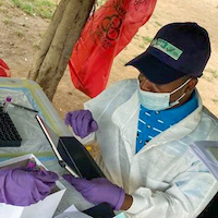 A person works with supplies. He wears a hat and purple gloves.