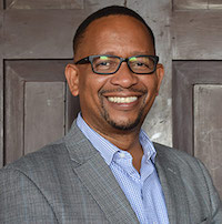 Thumbnail photo of a man wearing a grey suit jacket and glasses.