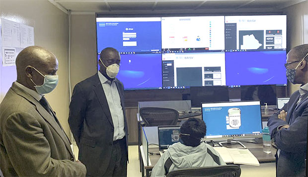 Four people wearing face masks stand in a circle looking at dashboard data.