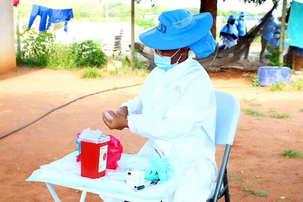 A person wearing a bright blue hat and P-P-E works at a small table.