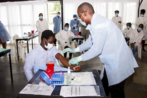 A person demonstrates drawing blood on another person while others watch.