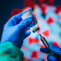 A syringe extracting vaccine from a vial.