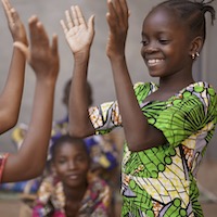 A girl wearing a green dress plays with another child with others look on.