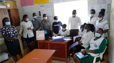 A group of people wearing masks sit in an office.