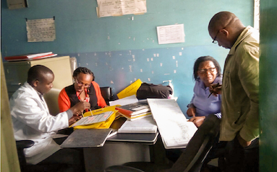 Four people work in two pairs of two. They look at books and are engaged with discussion. 