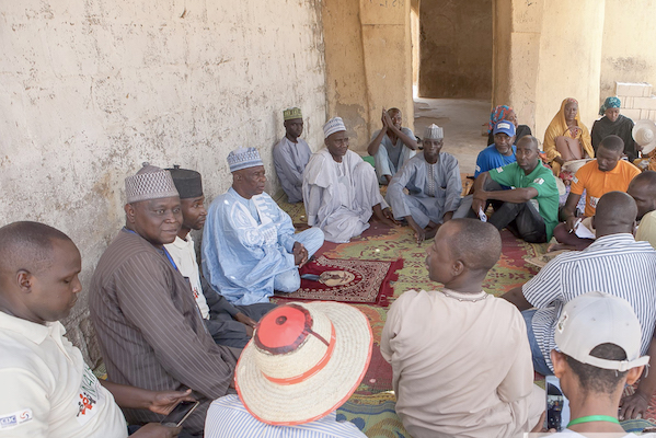 A large group of people sit on the ground in a circle.