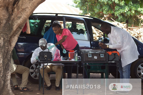 Two men and a woman have a work station set up outside next to a van.