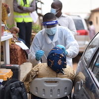 A field worker wearing protective equipment conducts a nasal swab of a woman sitting down.