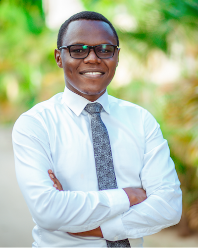 A man wearing glasses and a shirt and tie smiles. 