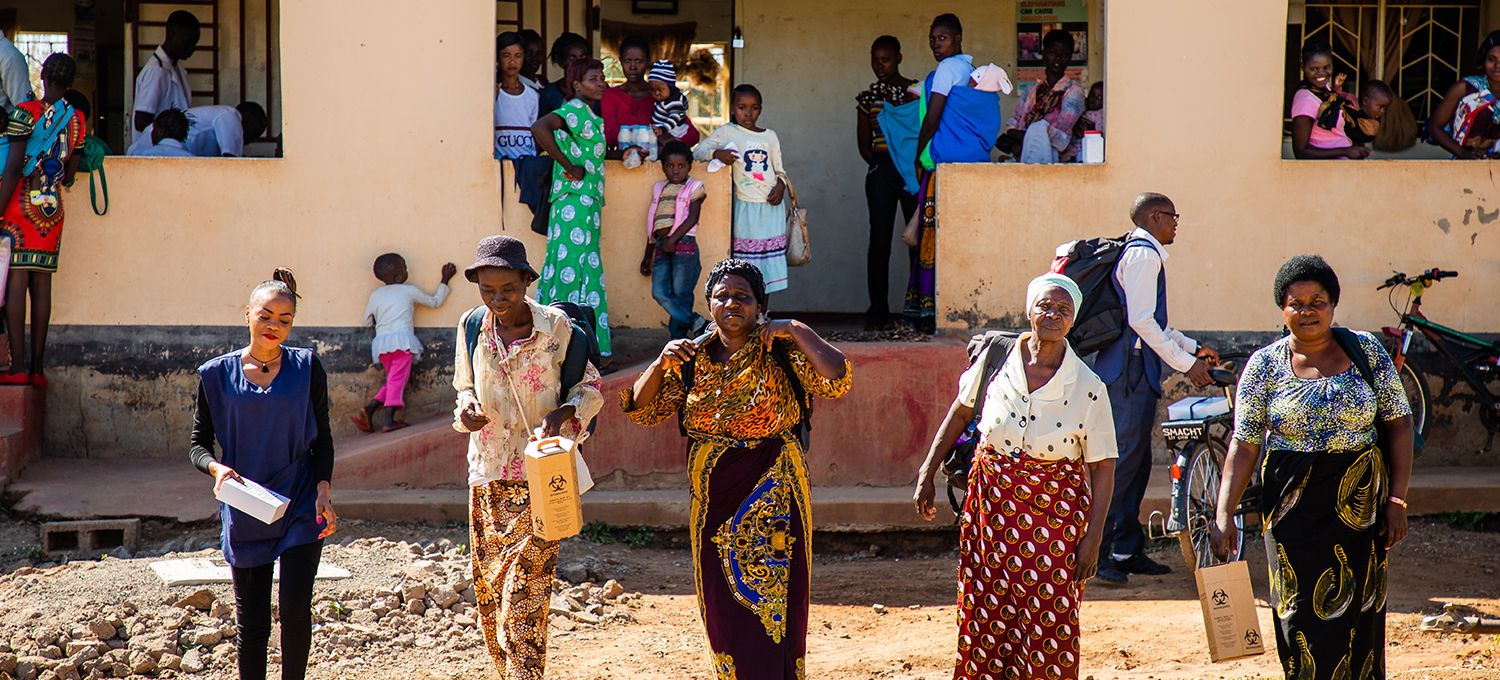 Five women stand in the foreground leaving a building with many people standing around it.